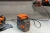 Adapter akumulatorowy Husqvarna 40-USB150X w kolorze pomarańczowym, widoczny w komplecie z akumulatorem Husqvarna.
