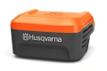 Adapter akumulatorowy Husqvarna 40-USB150X w kolorze pomarańczowym, widoczny napis Husqvarna oraz czarna podstawa. Produkt na jasnym tle.