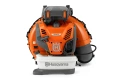 Zbliżenie dmuchawy Husqvarna 590BTS, w kolorze pomarańczowym i czarnym. Widoczne logo Husqvarna, obudowa filtra powietrza oraz zbiornik paliwa. Uchwyt ma ergonomiczną teksturę, co ułatwia trzymanie. Tło jest jednolite, jasne