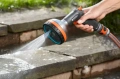 Premium pistolet zraszający wielofunkcyjny Gardena z ergonomicznym uchwytem i okrągłą końcówką. Ujęcie z boku, w tle widać elemanty ogrodu.