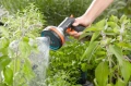 Premium pistolet zraszający wielofunkcyjny Gardena z ergonomicznym uchwytem i okrągłą końcówką. Ujęcie z boku, w tle widać kwiaty oraz drzewka. Kobieta prowadzi rynnę do podlewania roślin.
