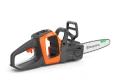 Pilarka akumulatorowa Husqvarna 215i w kolorze pomarańczowym z szarymi elementami, w ujęciu bocznym. Widoczna łańcuchowa układanka z logo Husqvarna, ergonomiczny uchwyt oraz przycisk uruchomienia. Produkt leży na ciemnym tle.