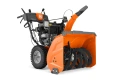 Odśnieżarka ST376 Husqvarna w kolorze pomarańczowym, frontalnie zmontowana, z metalową, szeroką turbiną do odśnieżania. Widoczne gumowe koła oraz ergonomiczne uchwyty. Silnik spalinowy, z czytelnym logo Husqvarna na uchwycie.