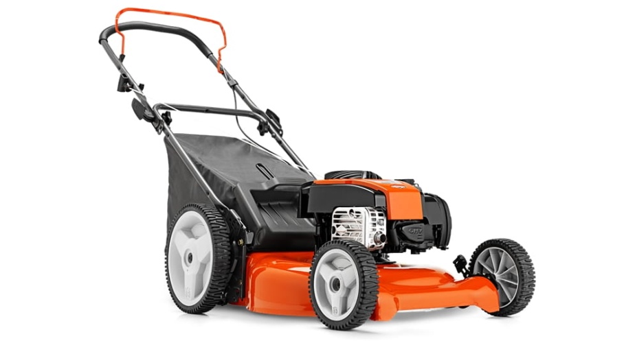 Kosiarka Husqvarna LC153 w kolorze pomarańczowym i czarnym, widoczna z boku, stojąca na twardej powierzchni. Ma szerokie koła oraz regulowaną rączkę. Widać silnik oraz przestronny zbiornik na trawę. Tło proste w odcieniach szarości.