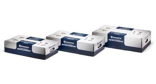 Zestaw instalacyjny Automower® Husqvarna z trzema niebiesko-białymi pudełkami, większe po lewej. Widać napisy INSTALLATION KIT i logo Husqvarna na prostym tle podkreślającym opakowanie.