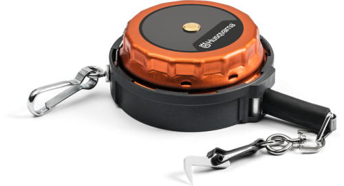 Taśma miernicza do drzew 15m Husqvarna w obudowie z czarnego tworzywa z metalowym, pomarańczowym pokryciem. Zwinięta, z karabińczykiem oraz metalowym haczykiem do zaczepienia. Widoczne logo Husqvarna na czarnej powierzchni.