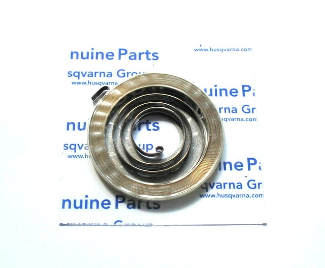 Sprężyna rozrusznika pilarki Partner P340S, metalowa, w kształcie sprężyny, na białym tle z niebieskimi napisami genuine Parts. Zbliżenie na kilka okręgów o równomiernej szerokości, jeden z końców przytwierdzony do podstawy.