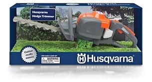 Zabawka nożyce do żywopłotu Husqvarna, szaro-pomarańczowe, z realistycznymi detalami, rączką, LED i etykietą z logo na zielonym tle.