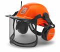 Kask Functional z radiem FM Husqvarna w intensywnym kolorze pomarańczowym. Ujęcie z boku, z ochronnym wizjerem i nausznikami. Widoczne logo na froncie kasku oraz siatkowa osłona twarzy. Kask zamontowany w pozycji na stojąco.